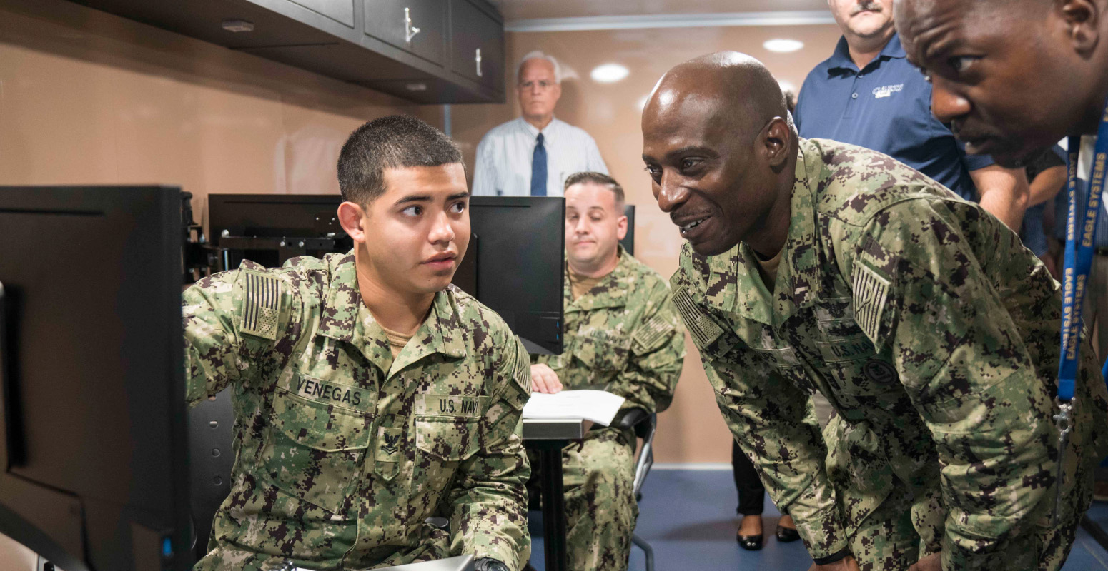 Navy personnel standing around a computer learning from levels 14